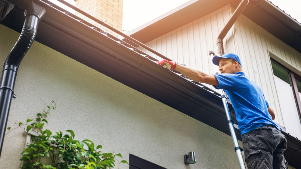 man on a ladder cleaning leaves, dirt and debris out of roof guttters